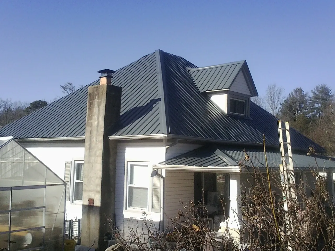 Dark blue standing seam metal roof on a white farmhouse with dormer — Slate & Tile Roof Repair by Roofing Brothers in Danby