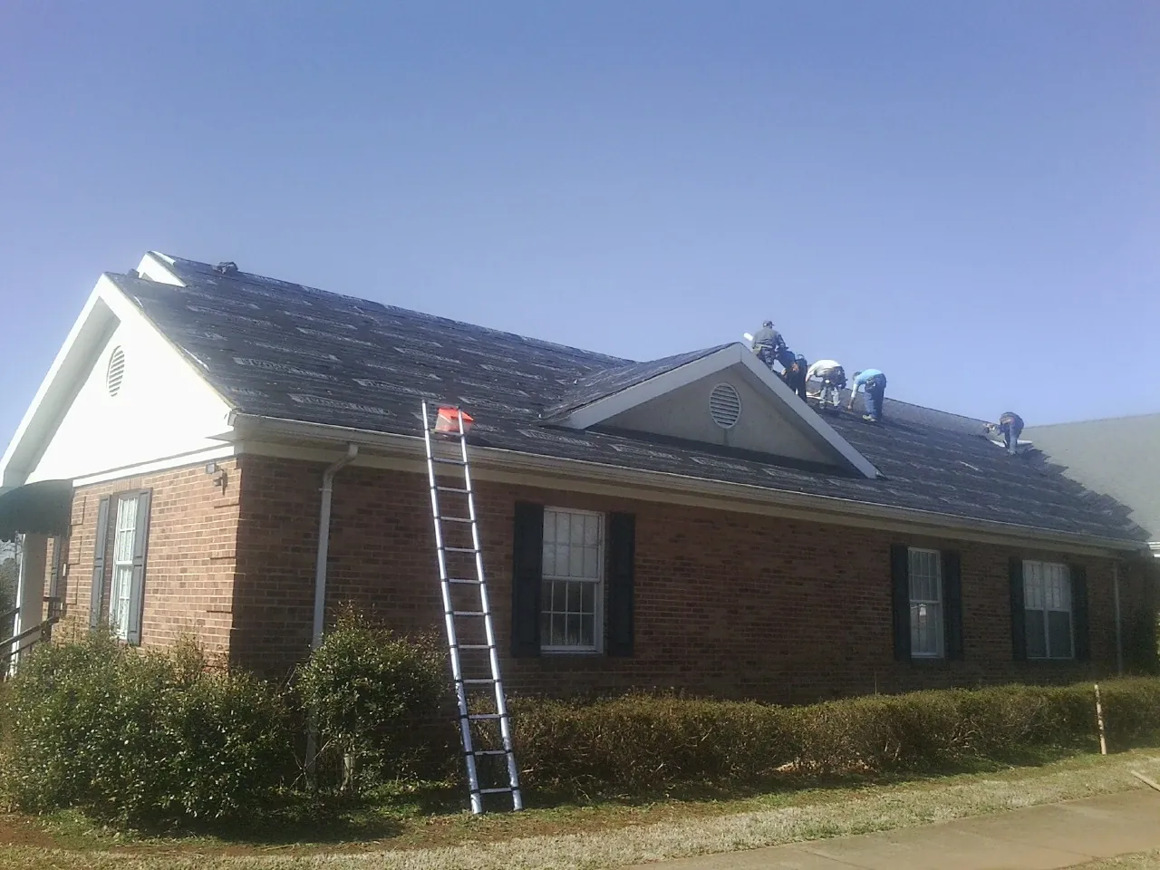 Crew tearing shingles off a brick ranch roof with a ladder set — Metal Roof Repair work by our crew in Danby