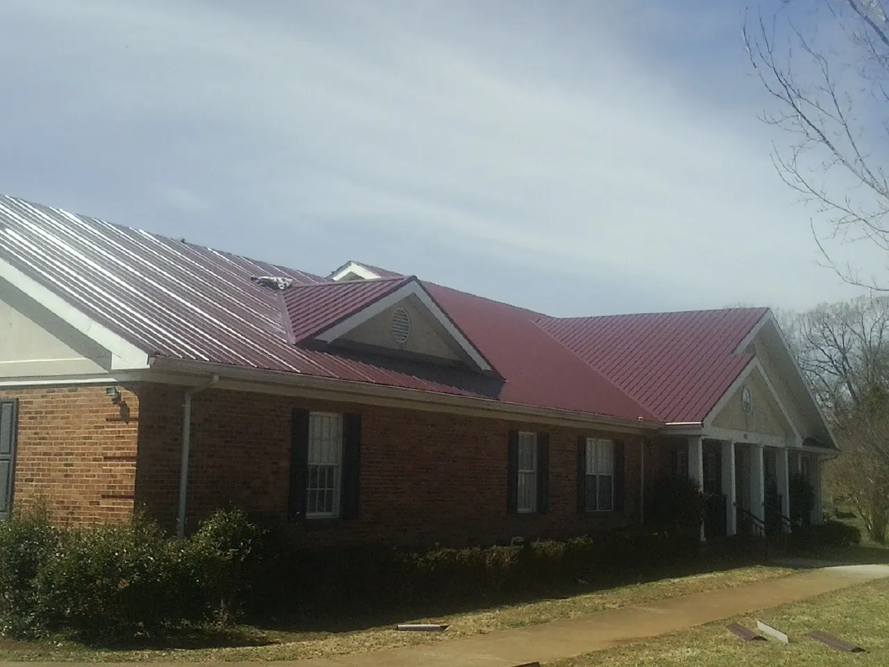 Red metal roof with gabled entries on a long brick building, from a Hail Damage Roof Repair job in Danby