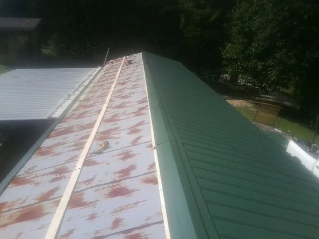 Old rusted panels beside newly installed green metal roofing — Wind Damage Roof Repair by Roofing Brothers in Danby