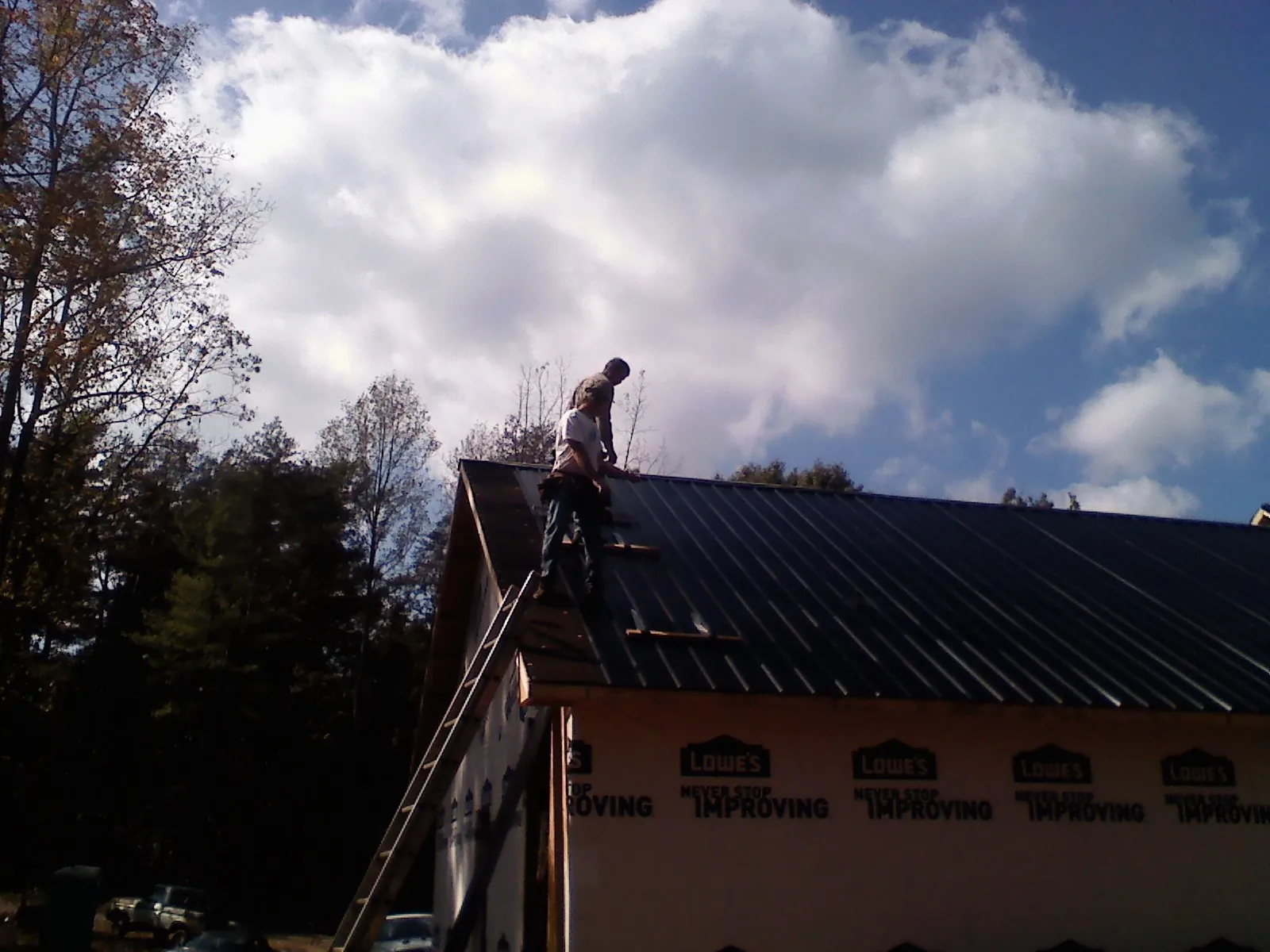 Roofer fastening dark metal panels high against a cloudy sky, from a Roof Inspection job in Danby