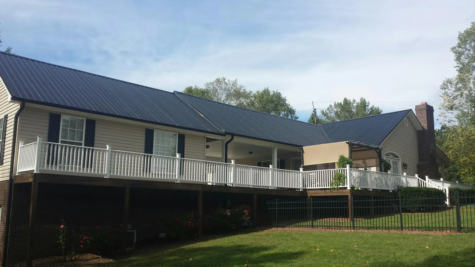 Black metal roof above a long white railed deck on a hillside home in Danby